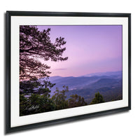 a breathtaking view of a mountainous landscape at sunset, with the sky painted in shades of purple and pink. The silhouettes of trees and mountains can be seen in the foreground, creating a sense of depth and vastness. The overall composition is visually striking and evokes a sense of tranquility and natural beauty.
