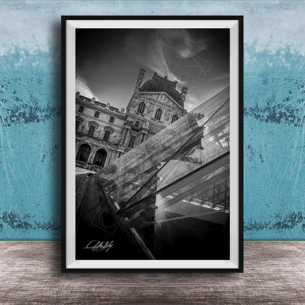 A black and white photograph of the Louvre Museum in Paris, France, with a modern glass structure in the foreground.