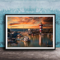 a serene harbor scene at sunset, with boats docked in the calm waters and a lighthouse standing tall in the background.