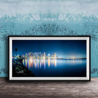 A framed photograph of a city skyline at night, with the city's lights reflected in the water below.