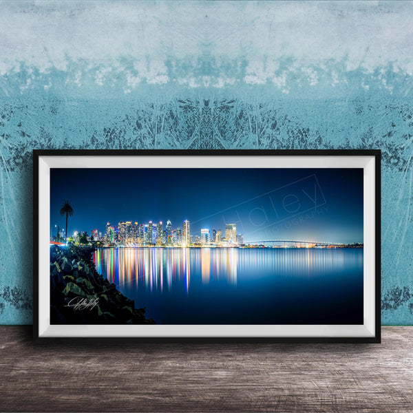 A framed photograph of a city skyline at night, with the city's lights reflected in the water below.