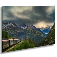 A train travels through a mountainous landscape, with snow-capped peaks and a dramatic cloudy sky in the background.