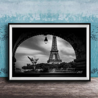 A black and white photograph of the Eiffel Tower in Paris, France, framed and displayed on a wooden surface against a blue textured wall.