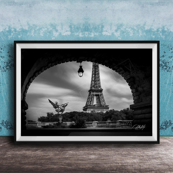 A black and white photograph of the Eiffel Tower in Paris, France, framed and displayed on a wooden surface against a blue textured wall.