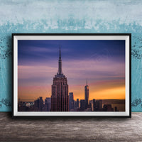 A framed photograph of the New York City skyline at sunset, with the Empire State Building prominently visible in the center of the frame.