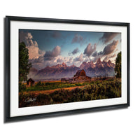 a picturesque rural landscape with a large barn, a wooden shed, and a mountain range in the background, all set against a colorful sky with clouds.