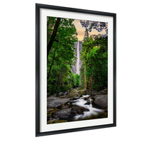 A framed photograph depicting a serene waterfall cascading through a lush, forested landscape.