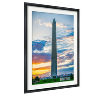 a tall obelisk against a colorful sunset sky, with a grassy area and some buildings in the background.
