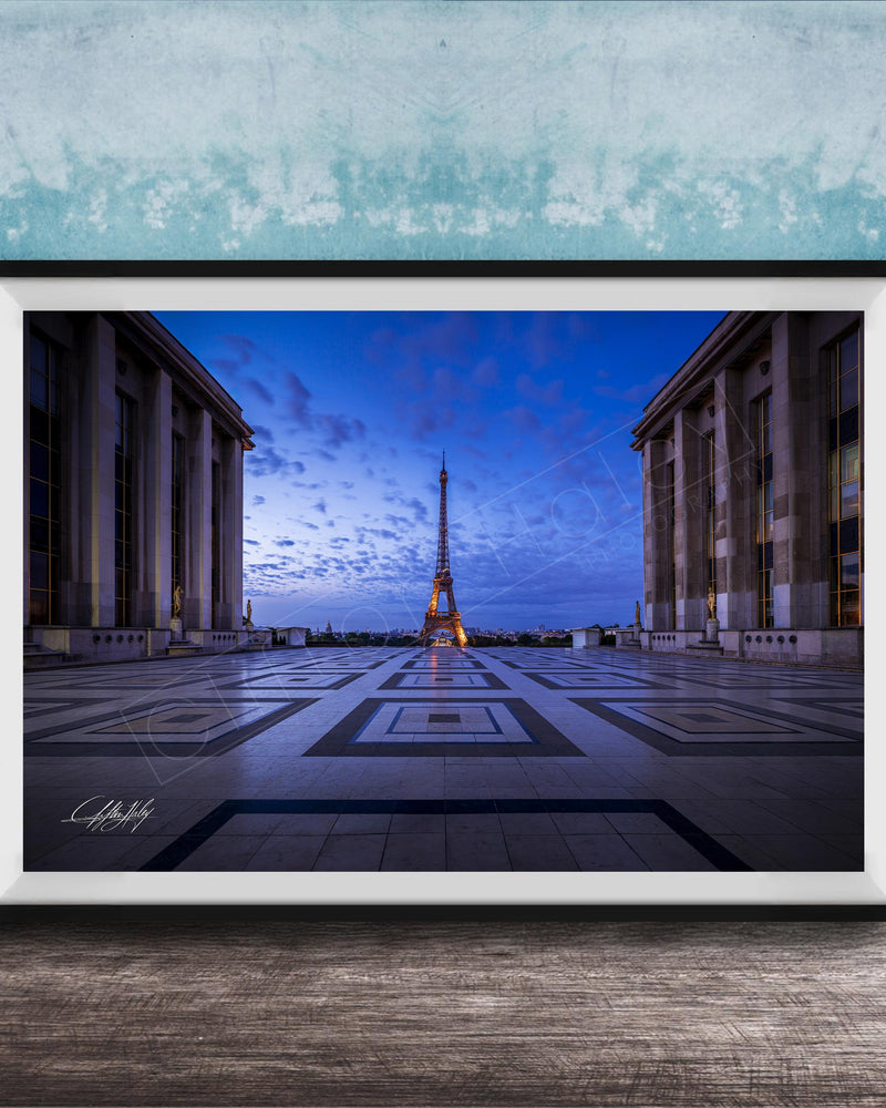 a large, framed photograph of the Eiffel Tower in Paris, France, with the tower illuminated against a blue sky.
