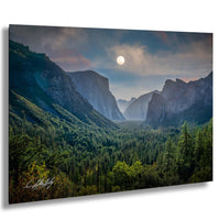 a breathtaking mountainous landscape with a full moon illuminating the scene. The mountains are covered in lush green trees, creating a serene and tranquil atmosphere. The sky above is a beautiful shade of blue, dotted with wispy clouds. The full moon casts a soft, ethereal light over the scene, enhancing the overall beauty of the landscape.