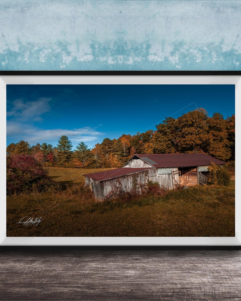 a rustic wooden barn nestled in a lush, green landscape with trees displaying autumn colors.