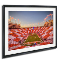 A framed photograph of a football stadium at dusk, with the field illuminated and the stands filled with spectators.