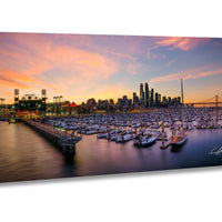 A panoramic view of a city skyline at sunset, with a marina filled with boats in the foreground.
