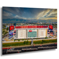 a large stadium with a red roof, surrounded by mountains and a cloudy sky.