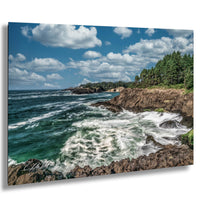 a rocky coastline with crashing waves, surrounded by a blue sky with white clouds.