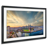 The image is a framed aerial view of a city skyline at sunset, with the city's buildings and landmarks illuminated against a colorful sky.