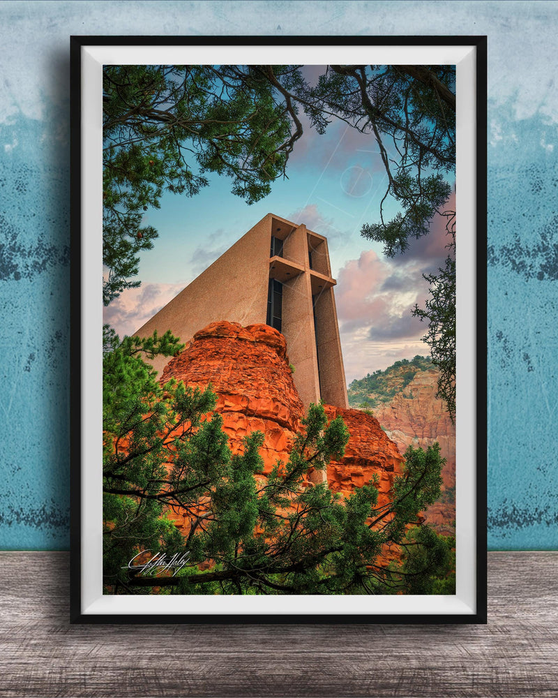 A framed photograph of a large, modern church with a distinctive cross-shaped roof, set against a backdrop of red rock formations and lush greenery.