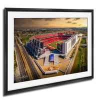 An aerial view of a large sports stadium with a red roof and white walls, surrounded by a cityscape.