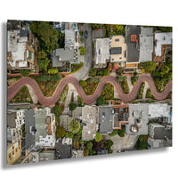 The image is an aerial view of a winding red road that curves through a residential neighborhood, with houses and trees lining the sides of the road.