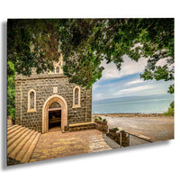 a stone church with arched windows and a stone pathway leading to the entrance. The church is surrounded by lush greenery, and the ocean can be seen in the background.
