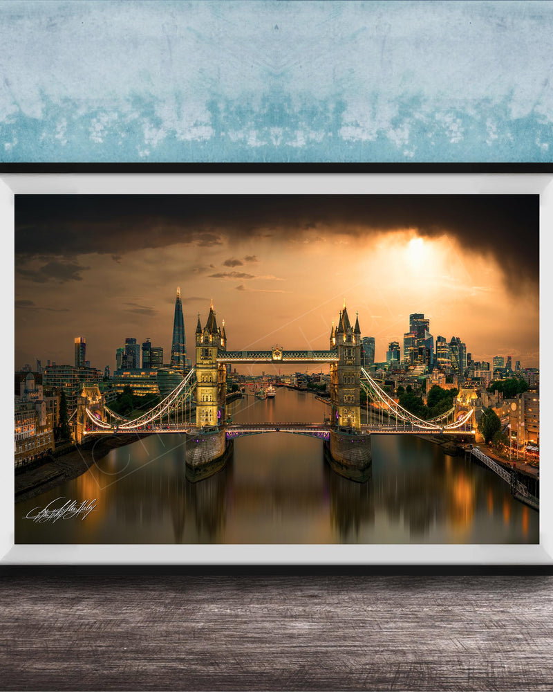 A framed photograph of the Tower Bridge in London, England, with the city skyline and the River Thames in the background, illuminated by a warm, golden glow.