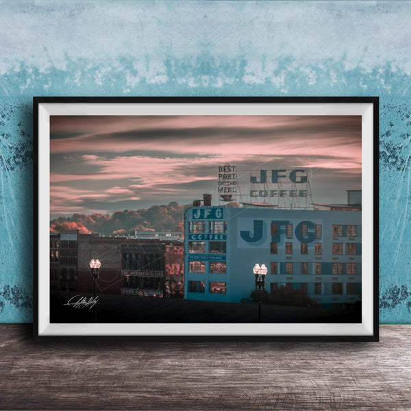 A framed photograph of a cityscape at sunset, with buildings and a sign for JFG Coffee prominently displayed.