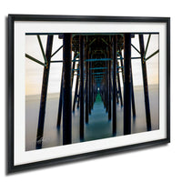 The image is a framed photograph of a long pier with wooden columns extending into the distance, creating a sense of depth and perspective.