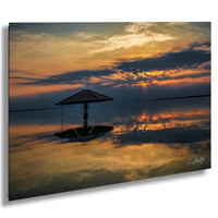 a serene sunset over a calm body of water, with a lone umbrella standing in the foreground.