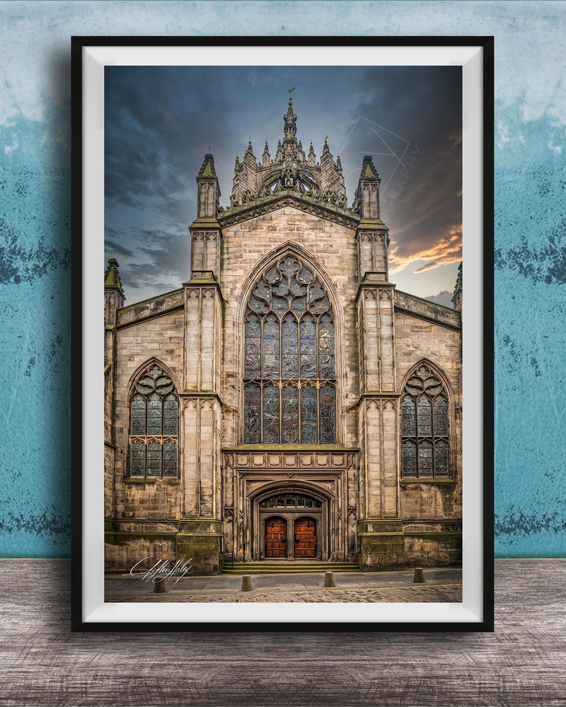 A framed photograph of a Gothic cathedral with a large rose window and a tall spire, set against a cloudy sky.