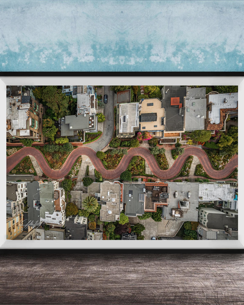 The image is an aerial view of a winding road in a residential area, with houses and trees lining the road.