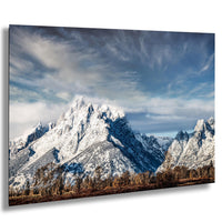 a majestic snow-capped mountain range under a cloudy blue sky, with a mix of green and brown vegetation in the foreground.