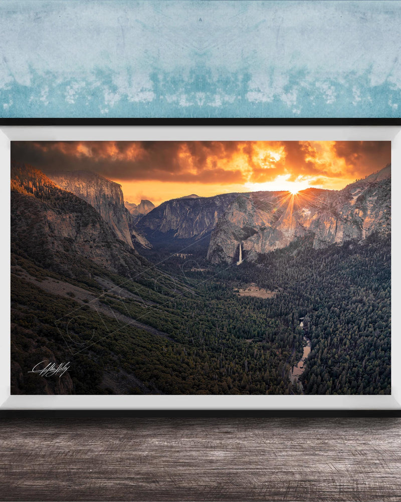 A framed photograph of a breathtaking mountain landscape at sunset, with the sun's rays illuminating the scene and casting a warm glow over the rugged terrain.
