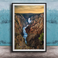 A framed photograph of a breathtaking waterfall cascading down a steep, rocky cliff face, with a vibrant sky in the background.