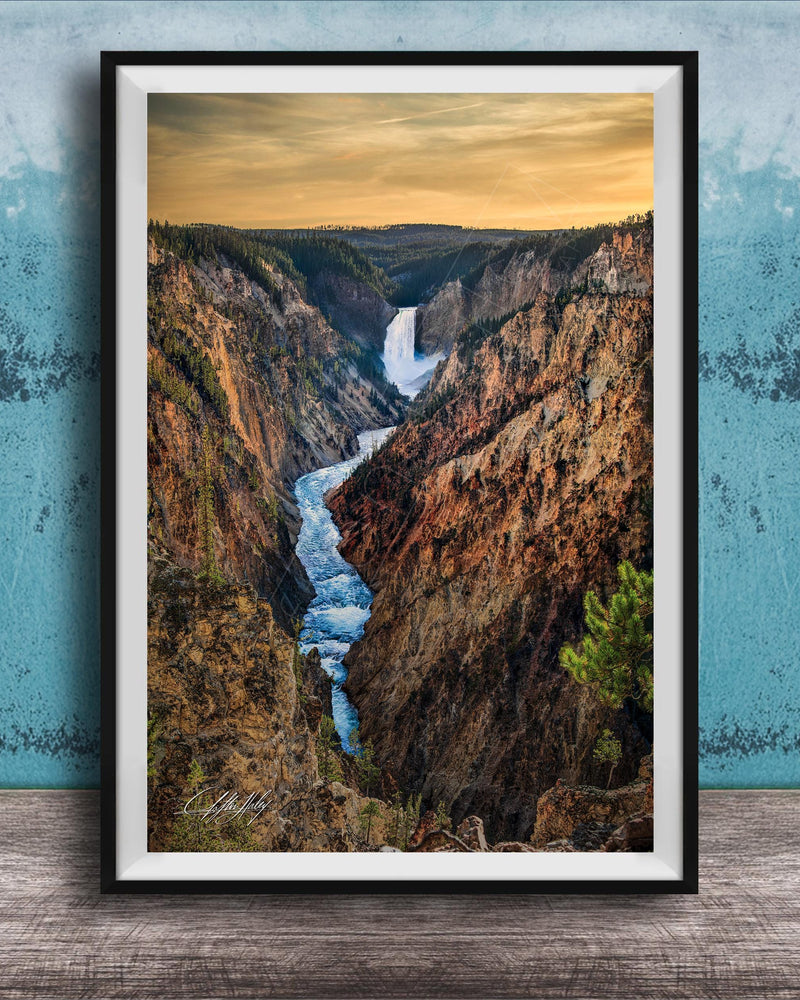 A framed photograph of a breathtaking waterfall cascading down a steep, rocky cliff face, with a vibrant sky in the background.