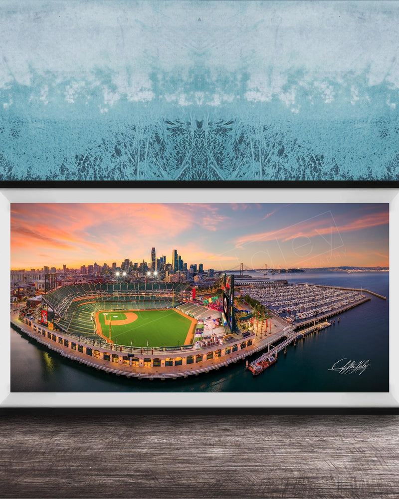 A framed aerial view of a baseball stadium and its surrounding cityscape at sunset.