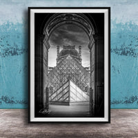 A framed photograph of the Louvre Museum in Paris, France, with the iconic glass pyramid structure prominently featured in the center of the frame.