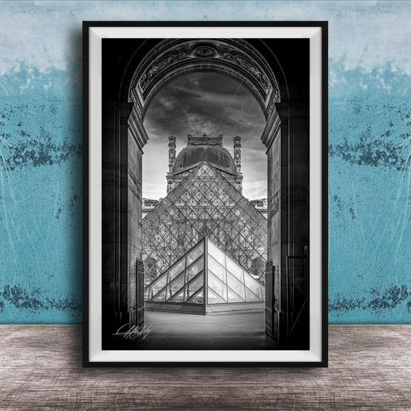 A framed photograph of the Louvre Museum in Paris, France, with the iconic glass pyramid structure prominently featured in the center of the frame.