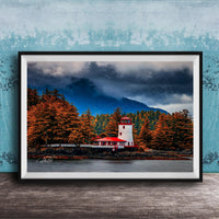A framed photograph depicting a lighthouse surrounded by a forest with autumn-colored trees, set against a cloudy sky.