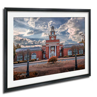 A framed photograph of a red brick building with a clock tower, surrounded by trees and a brick walkway.