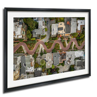 The image is an aerial view of a winding road that curves through a densely populated urban area, with buildings and greenery lining the sides of the road.