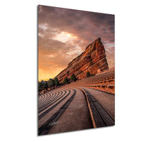 a large, steep rock formation with a curved, wooden walkway leading up to it, set against a dramatic sky with orange and pink hues.