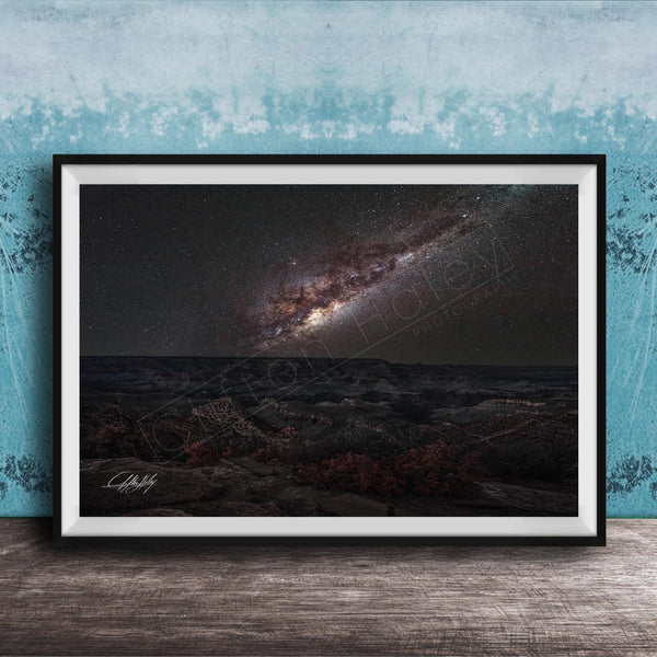 The image is a framed photograph of a night sky with a galaxy, placed on a wooden surface against a blue wall.