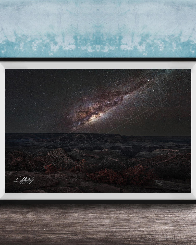 The image is a framed photograph of a night sky with a galaxy, placed on a wooden surface against a blue wall.