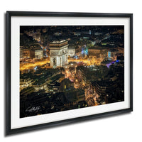The image is a framed photograph of a city at night, featuring a large, illuminated archway or monument in the center of the frame. The surrounding buildings and streets are brightly lit, creating a vibrant and lively atmosphere.