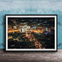 The image is a framed photograph of a city at night, featuring a large, illuminated archway or monument in the center. The cityscape is filled with numerous buildings and lights, creating a vibrant and bustling nighttime scene.