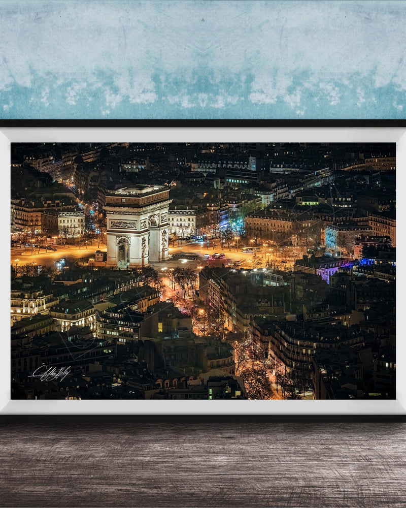 The image is a framed photograph of a city at night, featuring a large, illuminated archway or monument in the center. The cityscape is filled with numerous buildings and lights, creating a vibrant and bustling nighttime scene.