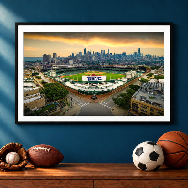A framed aerial view of a baseball stadium with a city skyline in the background, featuring a sports ball, a baseball glove, and a basketball on a wooden shelf below the frame.