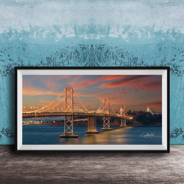 A framed photograph of the Golden Gate Bridge at sunset, with the bridge illuminated and its towers and suspension cables glowing against the colorful sky.