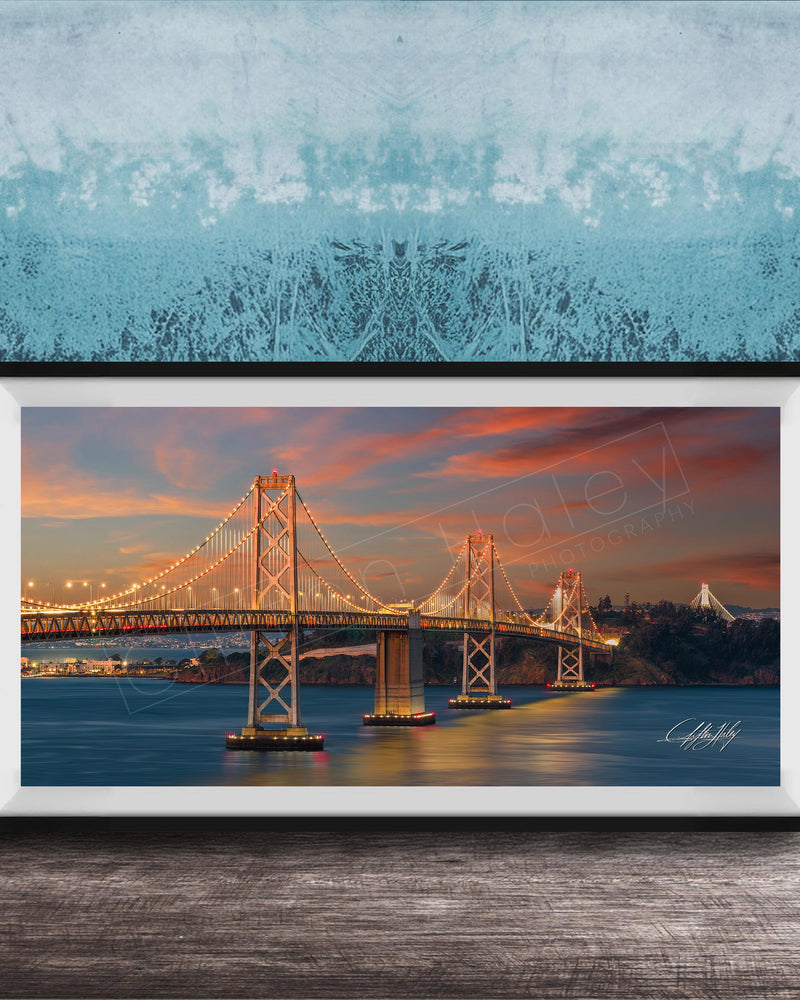 A framed photograph of the Golden Gate Bridge at sunset, with the bridge illuminated and its towers and suspension cables glowing against the colorful sky.