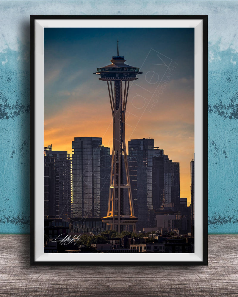 A framed photograph of the Space Needle in Seattle, with the city skyline in the background at sunset.